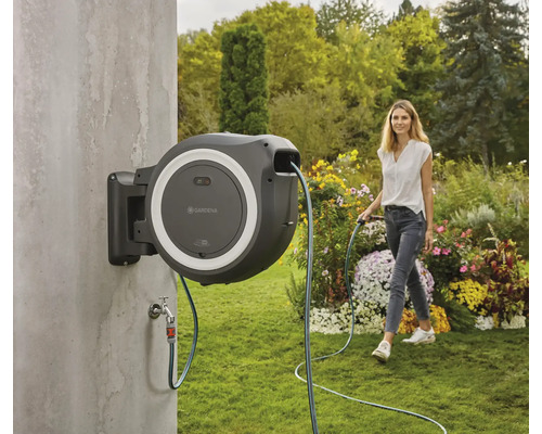 Scène de jardin avec une femme arrosant un jardin avec un tuyau d''arrosage fixé à un dévidoir.
