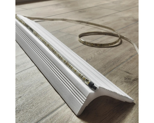 Weisse Zierleiste mit LED-Streifen auf einem Holzboden.