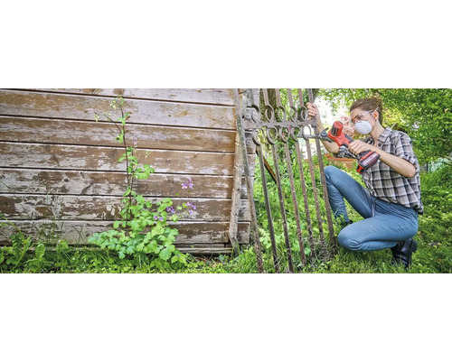 Frau arbeitet mit einem Multifunktionswerkzeug an einem Gartentor aus Metall. Sie trägt eine Schutzmaske und eine Schutzbrille.
