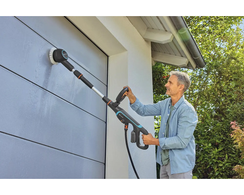 Un homme nettoie un mur avec une brosse et un manche télescopique