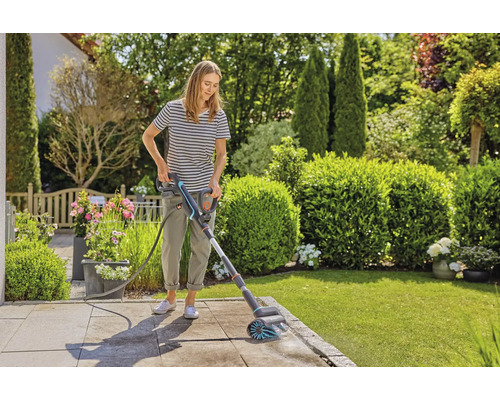 Une femme nettoie une terrasse avec une brosse électrique dans le jardin.