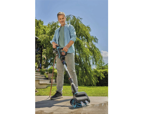 Un homme utilise une brosse Gardena pour nettoyer une surface en pierre à l''extérieur.