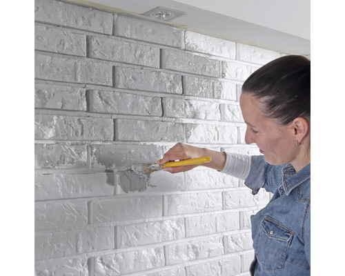 Frau streicht Ziegelwand mit Pinsel