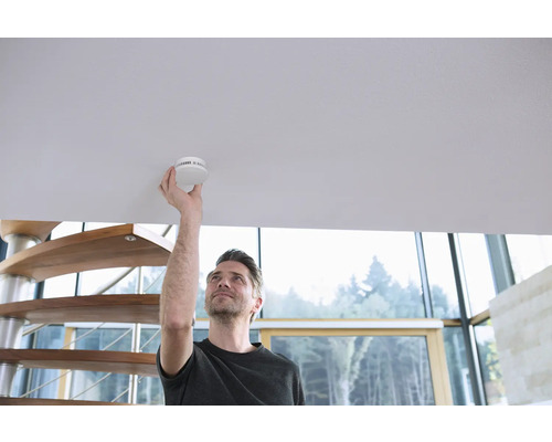 Un homme installe un détecteur de fumée au plafond