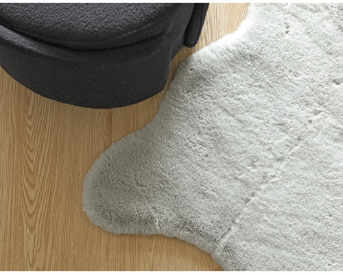 Vue détaillée d''un tapis gris imitation peau de mouton à côté d''un fauteuil sur un plancher en bois