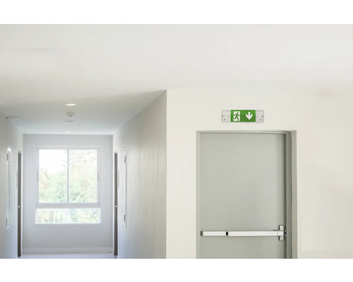 Couloir avec panneau de sortie de secours et porte avec barre anti-panique