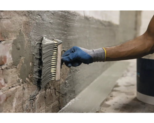 Un artisan applique un revêtement imperméable sur un mur avec une brosse.