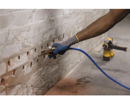 Homme injectant du liquide dans un mur de briques avec une lance d''injection