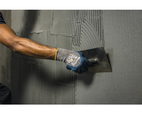 Fliesenleger trägt Kleber mit einer Kelle auf die Wand auf