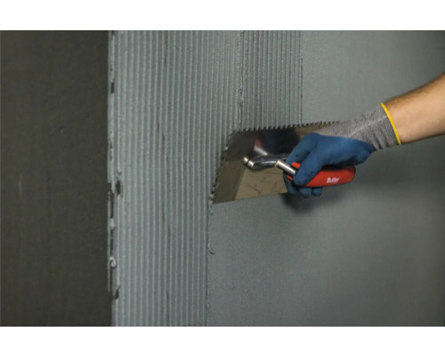 Fliesenleger trägt Fliesenkleber mit einer Glättkelle auf eine Wand auf