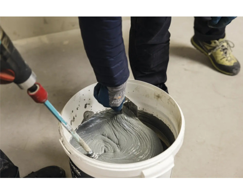 Fliesenkleber wird in einem Eimer mit einem Rührwerk und einer Spachtel gemischt.