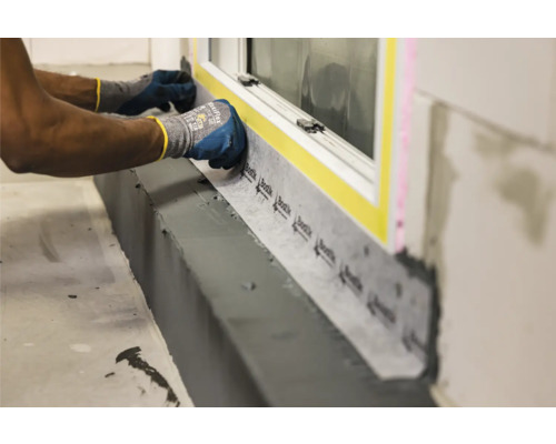 Anbringung einer Fensterabdichtung im Innenbereich mit Dichtband und Schutzhandschuhen.