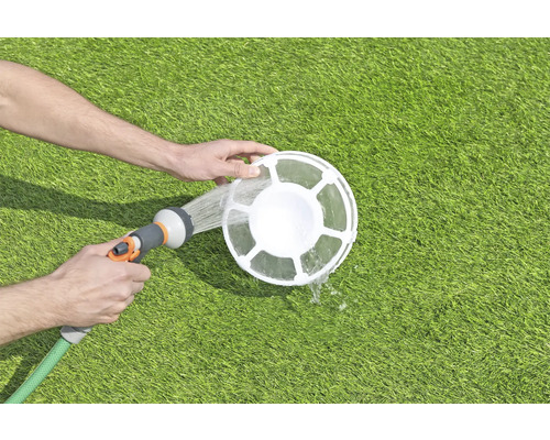 Nettoyage d''un skimmer de piscine avec un tuyau d''arrosage sur une pelouse.