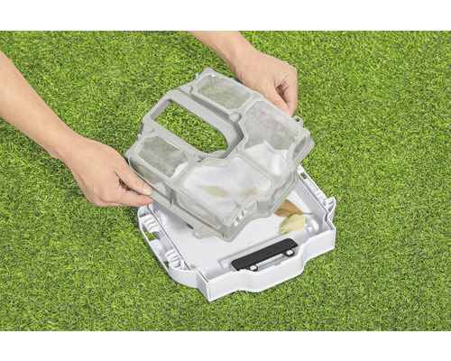 Une personne place un tamis dans un robot de piscine sur une pelouse verte