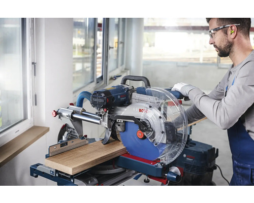 Scie à onglet coupant une pièce de bois, manipulée par un artisan