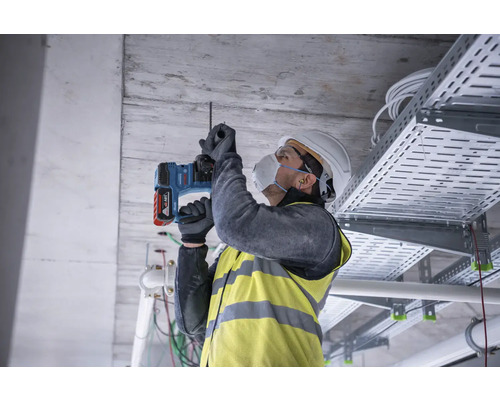Un artisan perce un trou dans le plafond avec un perforateur.