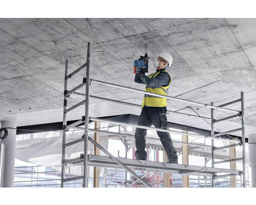 Artisan sur un échafaudage perçant le plafond avec un perforateur