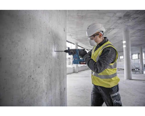 Un ouvrier perce un trou dans un mur en béton avec un perforateur.