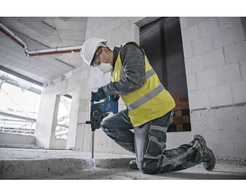 Un ouvrier du bâtiment est agenouillé et utilise un perforateur sur un chantier.