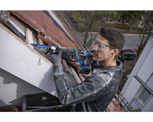 Un homme travaille avec une scie sabre sur un toit