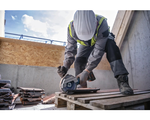 Un ouvrier du bâtiment coupe des tuiles avec une disqueuse sur une palette