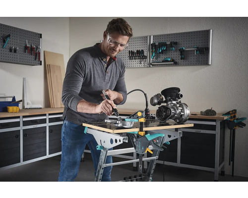 Un homme travaille avec un outil multifonctionnel sur une pièce sur un établi dans un atelier.
