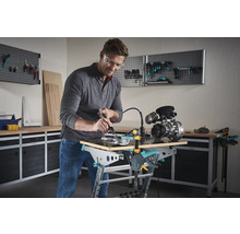 Un homme travaille avec une perceuse à main sur une pièce fixée avec des serre-joints sur un établi.