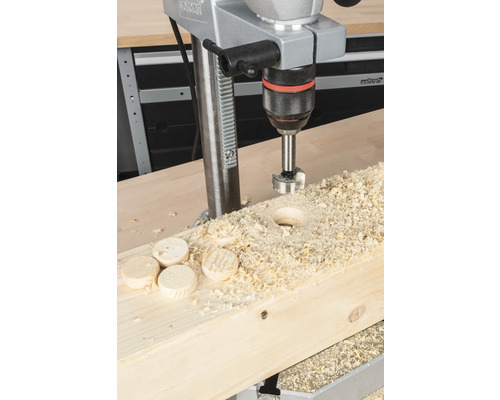 Perceuse à colonne perçant un trou dans une planche de bois avec des copeaux de bois et des disques de bois