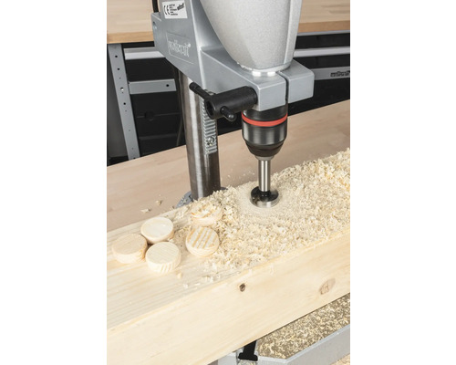 Perceuse perçant un trou dans une planche de bois, avec des copeaux de bois et des rondelles de bois