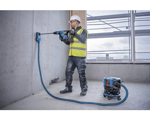 Handwerker bohrt mit Bohrhammer ein Loch in eine Betonwand mit Staubabsaugung
