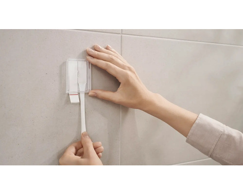 Frau befestigt Klebestreifen mit Spender an der Wand