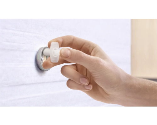 Eine Hand befestigt einen Spreizdübel an einer Wand.