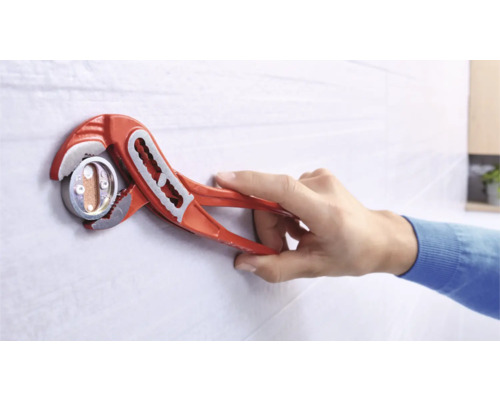 Eine Person verwendet eine Wasserpumpenzange, um eine Sanitärinstallation an einer Wand zu befestigen.