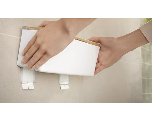 Une personne fixe une poubelle murale blanche au mur.
