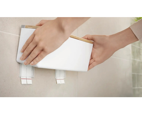 Une personne fixe un distributeur de savon mural blanc avec couvercle en bambou au mur