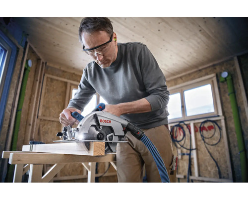 Ein Mann sägt ein Holzbrett mit einer Bosch Kreissäge in einem Holzhaus.