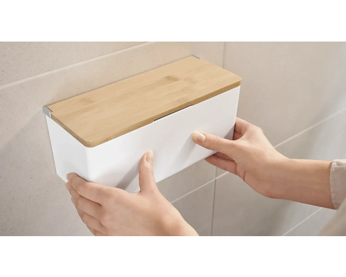 Une personne fixe un coffret mural blanc avec un couvercle en bambou sur un mur