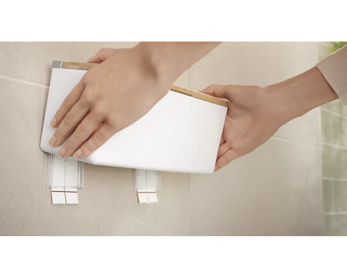 Une personne fixe un distributeur d''essuie-mains en papier blanc avec un couvercle en bambou au mur.