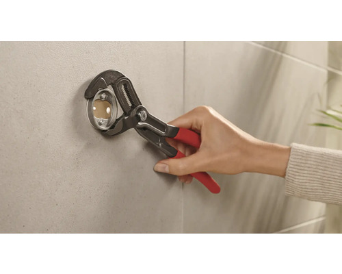 Installateur befestigt eine Rosette mit einer Rohrzange an einer Wand.
