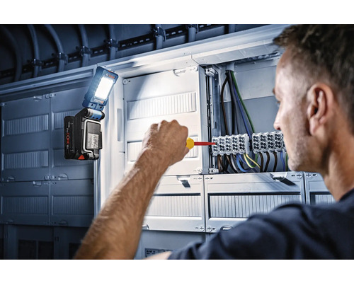 Un électricien travaille sur un tableau de distribution avec une lampe de travail Bosch.