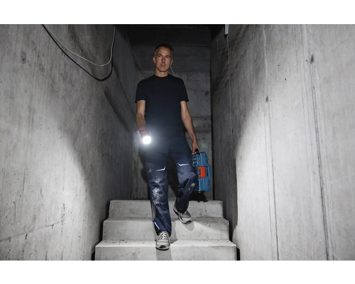 Homme descendant un escalier en béton avec une lampe de poche et une boîte à outils