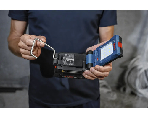 Un homme tient une lampe de travail à batterie avec crochet de la marque Bosch.