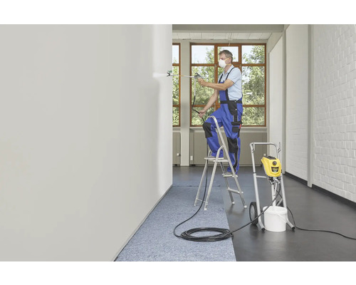 Un artisan portant un masque respiratoire peint un mur avec un pulvérisateur de peinture depuis une échelle.