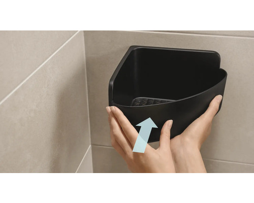 Eine Person befestigt ein schwarzes Eckregal im Badezimmer.