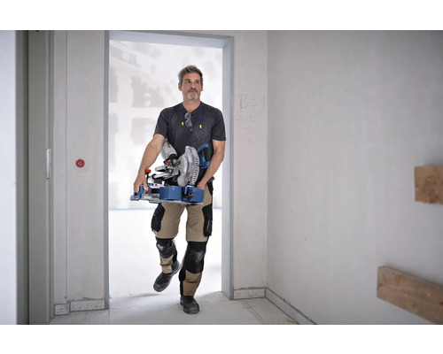 Mann trägt eine Kapp- und Gehrungssäge in einem unfertigen Raum