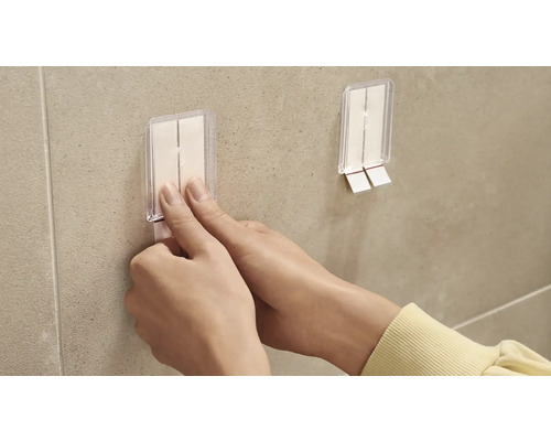 Eine Person befestigt einen Klebehaken an einer Wand