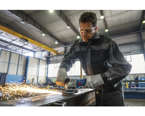 Ein Mann arbeitet mit einem Winkelschleifer an Metall und trägt dabei Schutzkleidung.