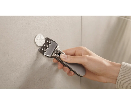 Eine Hand verwendet einen Schaber, um Klebereste von einer Fliese zu entfernen.