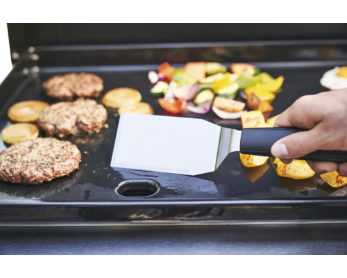 Plancha avec burgers, légumes et spatule en utilisation.