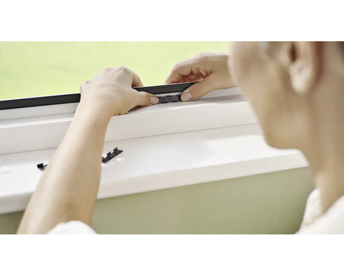 Une personne installe un écran anti-insectes sur une fenêtre